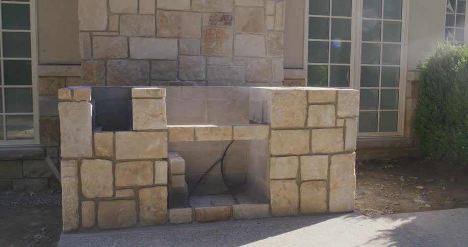 A slow zoom out of a custom stone outdoor kitchen and barbecue island under construction at a new residential home