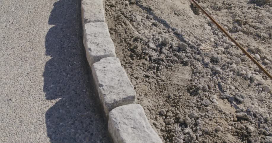 A newly installed curved granite cobblestone curb is set in concrete on a construction site