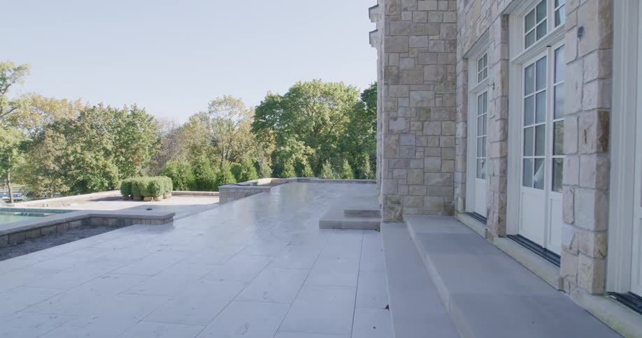 Slow dolly shot reveals a luxury stone patio and infinity pool overlooking a lake at a home under construction