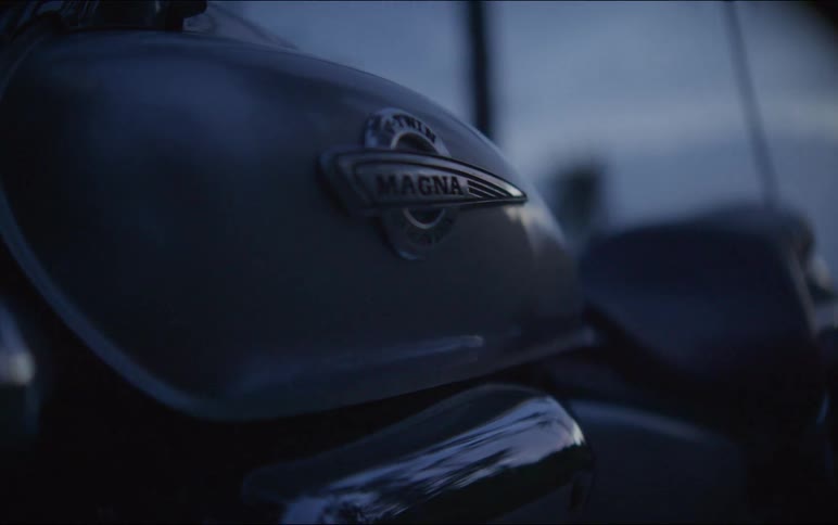 Close-up detail shot of a Honda Magna motorcycle gas tank emblem against a moody twilight sky