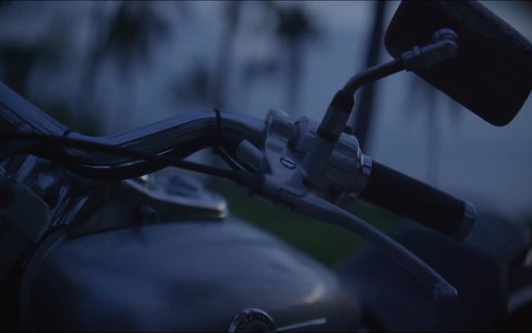 A moody close-up of a motorcycle's chrome handlebars and mirror at dusk