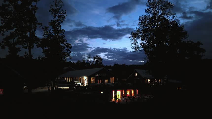 Dramatic clouds time-lapse over a cozy, lit-up rural retreat nestled in the woods at dusk