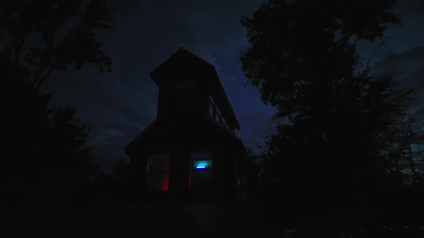 Slow zoom out from a mysterious house at night, its dark silhouette punctuated by colorful lights glowing from within