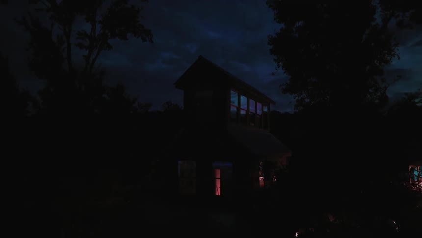 A time-lapse of a remote cabin at night shows colorful lights changing in the windows as clouds pass overhead