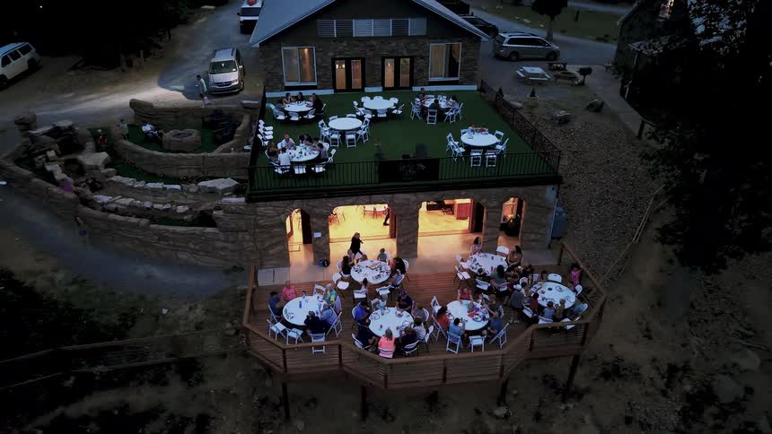 A high-angle timelapse captures guests enjoying a festive evening dinner party on the outdoor patios of a beautiful rustic venue