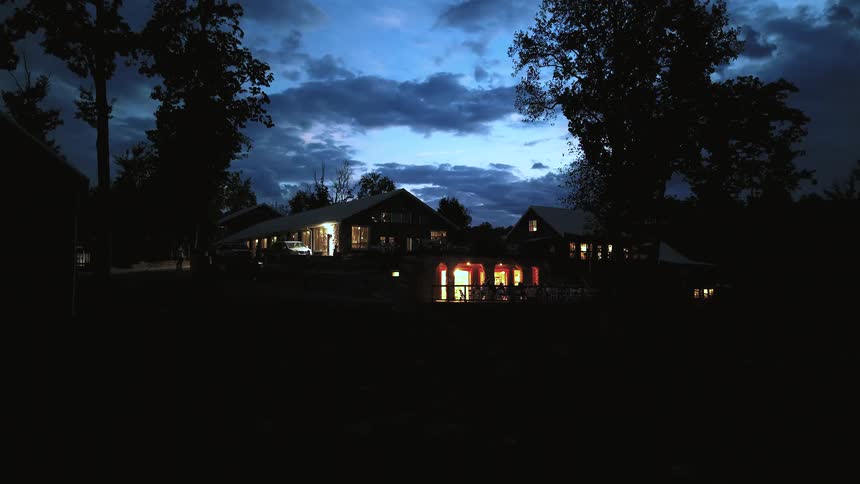 An aerial shot pulls back to reveal a beautiful, warmly lit rustic lodge and event venue at dusk