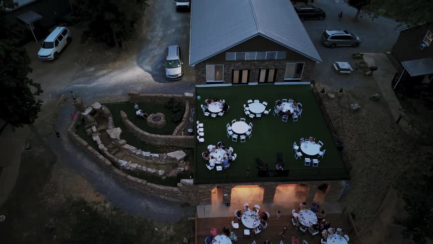 Aerial pullback shot of guests celebrating at a multi-level outdoor wedding reception at dusk