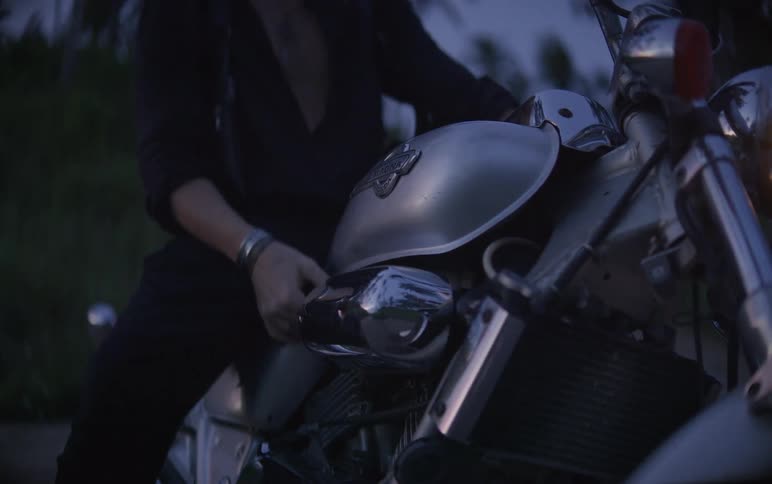Close up of a biker getting off a silver chopper motorcycle at twilight before walking away