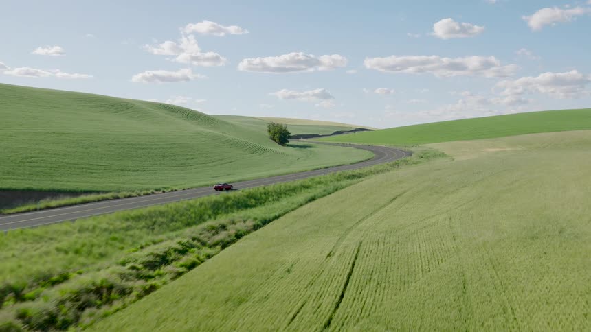 An aerial shot follows a red sports car driving along a winding road through the beautiful green rolling hills of the countryside