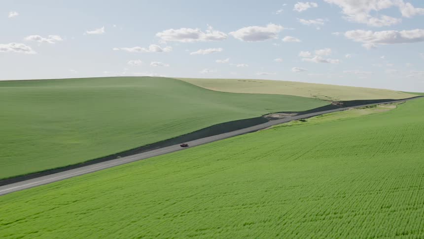 Aerial view of a red car driving along a scenic road through the vast, rolling green hills of the countryside