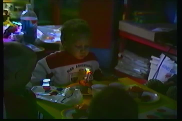 Vintage home movie captures a young boy blowing out the number 4 candle on his birthday cupcake at a party