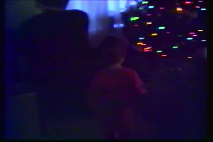 Vintage VHS footage captures a young boy in red pajamas walking into the living room to discover presents under the Christmas tree