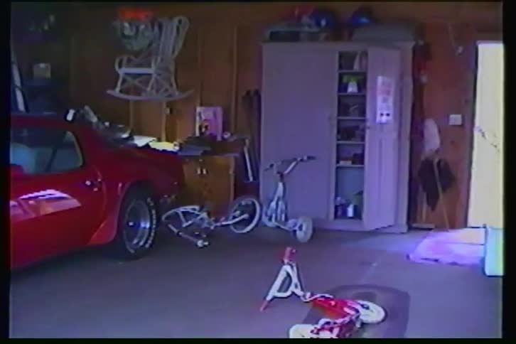 Home video footage from the 1980s slowly pans across a cluttered garage featuring a classic red Pontiac Trans Am