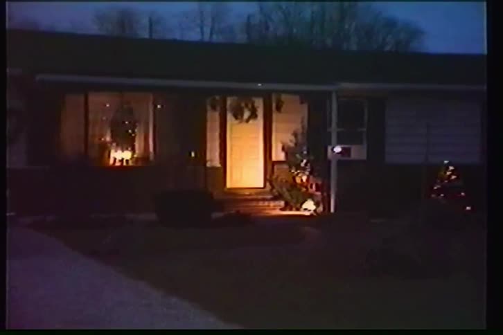 A slow zoom into a cozy suburban home decorated for Christmas at dusk, captured on vintage home video