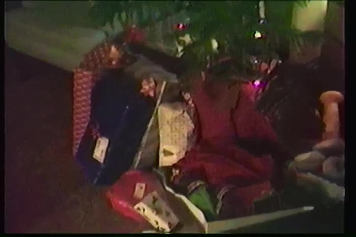 A nostalgic VHS tilt-down shot reveals a lit Christmas tree with presents and stockings underneath
