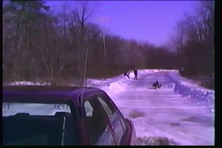 Nostalgic VHS footage from the 1990s captures kids joyfully sledding down a long, snow-covered hill