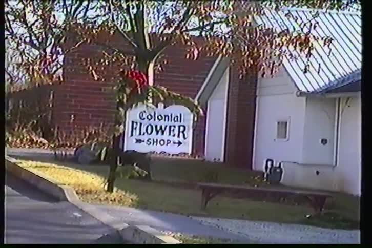 Nostalgic VHS home video footage from the 1980s pans across a small town 'Colonial Flower Shop' sign