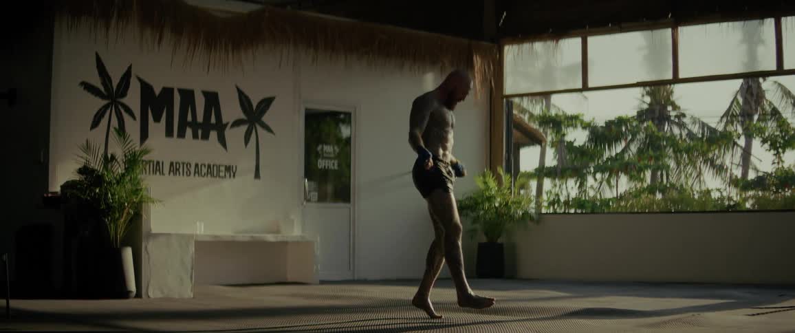 A tattooed man jump ropes barefoot in a tropical martial arts academy during his workout routine
