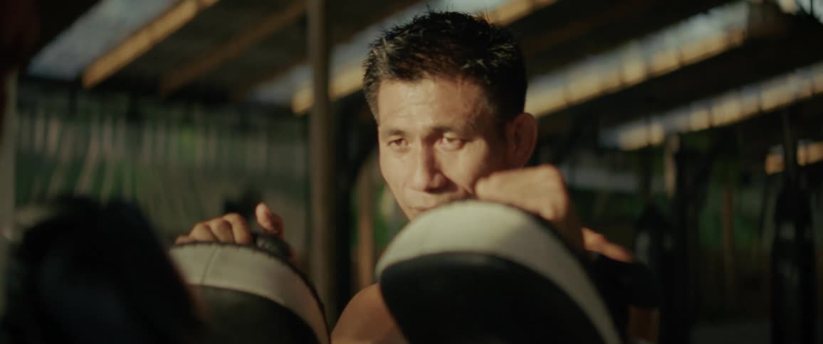 A focused boxing coach absorbs punches on his pads from a fighter's perspective in a dramatic slow-motion close-up