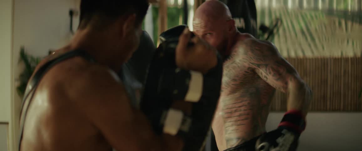 Slow motion shot of a tattooed fighter powerfully training with his coach in a gritty, open-air boxing gym