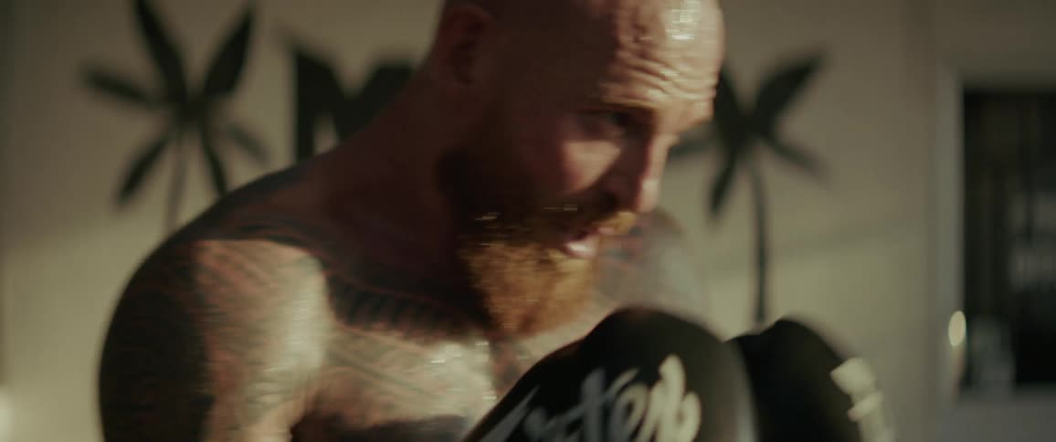 Intense slow-motion close-up of a tattooed and bearded MMA fighter shadowboxing in a gym