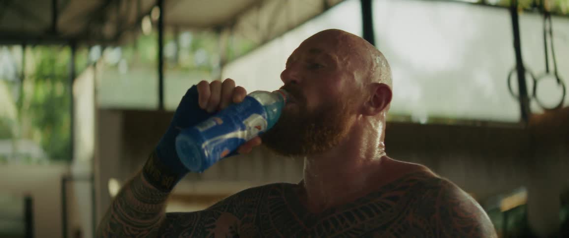 A sweaty tattooed fighter takes a break from his workout to drink a refreshing sports drink in slow motion