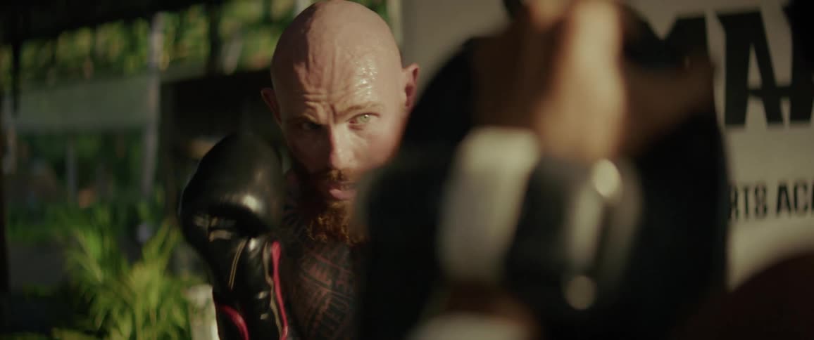 Intense slow-motion close-up of a sweaty, tattooed fighter with a red beard training with boxing pads