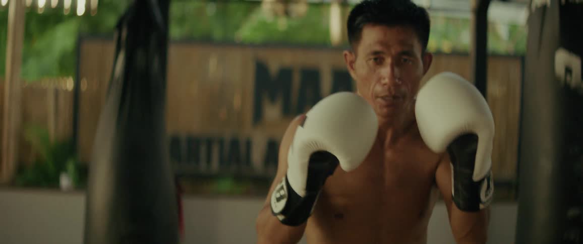 An intense martial arts fighter wearing boxing gloves practices his punches in slow motion at an outdoor training gym