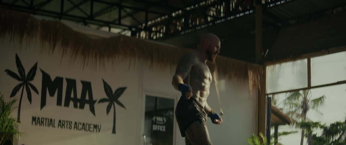 A heavily tattooed MMA fighter warms up with a jump rope in slow motion at a tropical martial arts academy