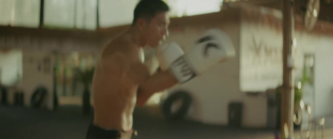 A focused and muscular Muay Thai fighter practices a powerful combination of punches and kicks while shadowboxing in a rustic, open-air gym