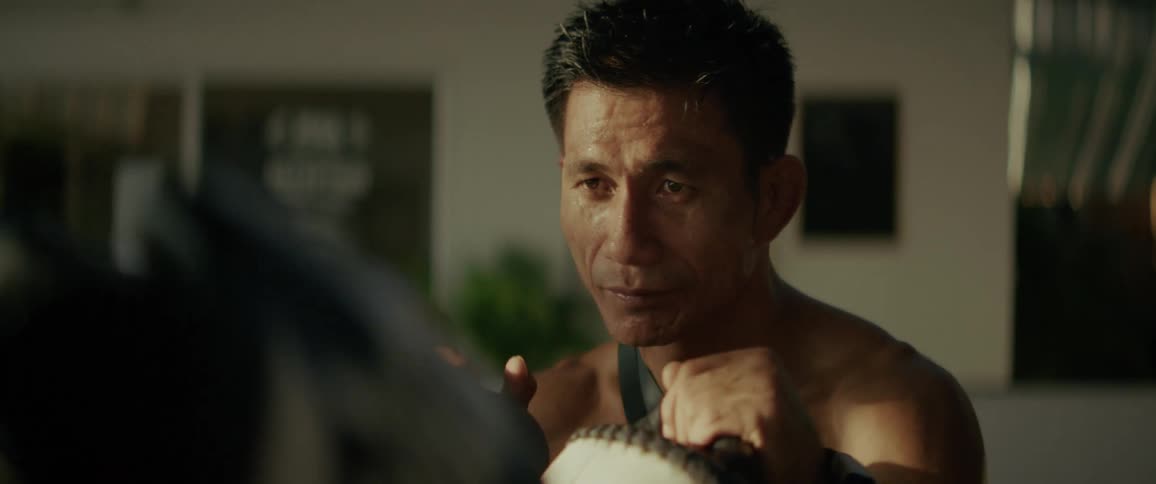 A focused martial arts coach holds pads for a fighter during an intense, slow-motion training session