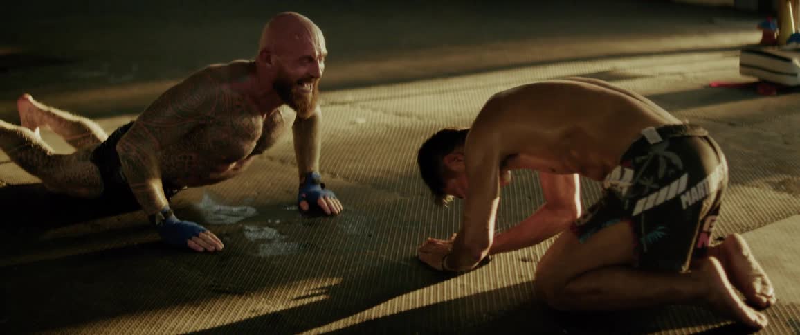 A tattooed fighter and his coach show respect after a grueling workout, bowing and finishing with a handshake and a hug