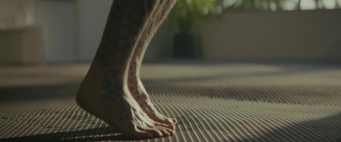 Slow-motion close-up of a tattooed man jumping rope barefoot, tilting up from his feet to his muscular body