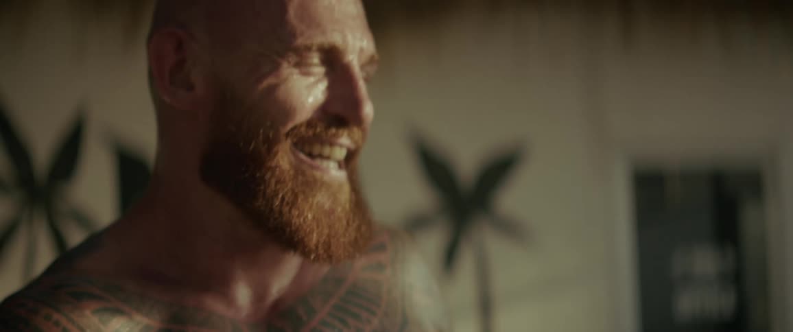 Slow motion close-up of a sweaty, tattooed boxer laughing before putting on his gloves and becoming serious