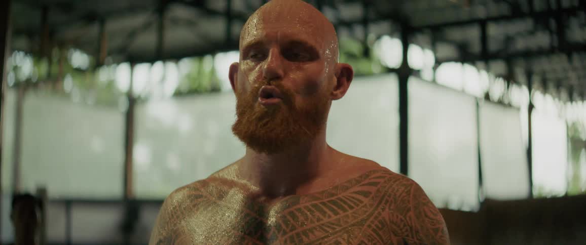 A slow-motion close-up shows a heavily tattooed fighter with a red beard catching his breath after an intense workout