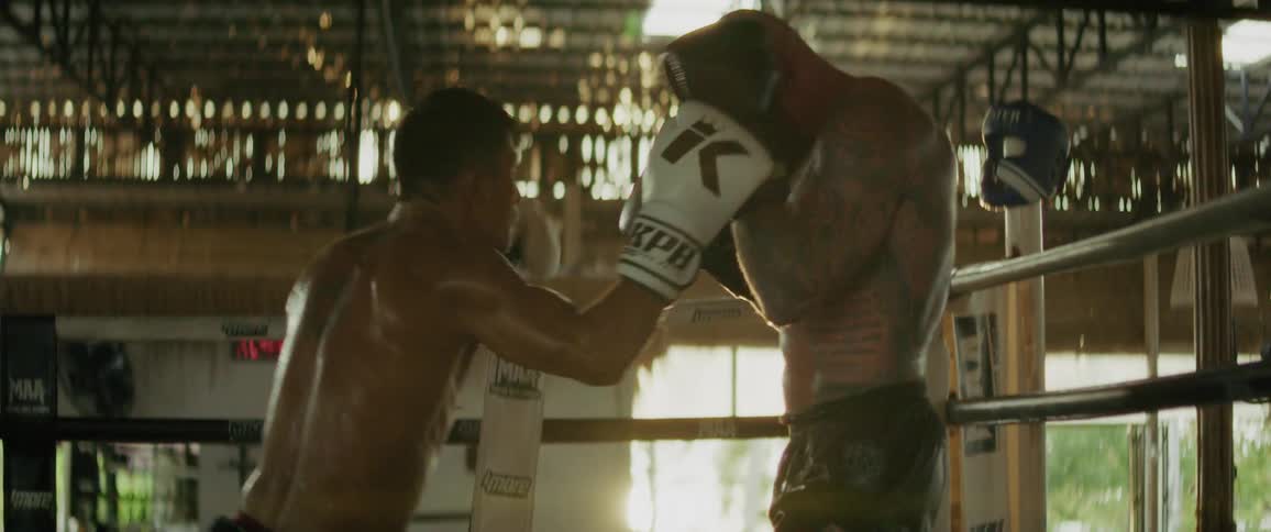 Two male kickboxers spar intensely in slow motion inside a sun-drenched, gritty boxing ring