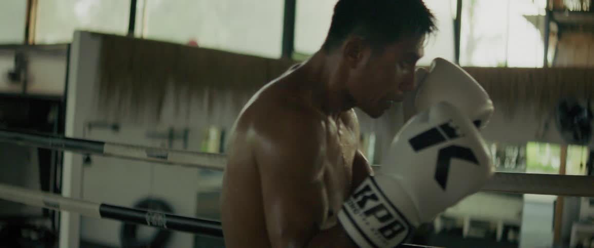 Two muscular male boxers trade powerful punches during an intense slow-motion sparring match inside a rustic gym