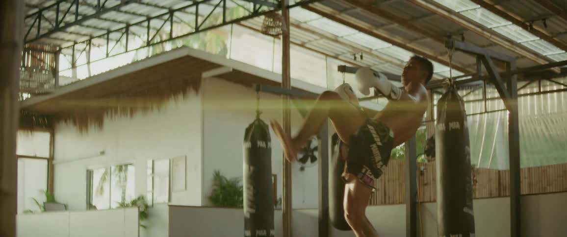 A powerful martial artist practices his impressive kicks and punches while training in a sunlit gym in slow motion