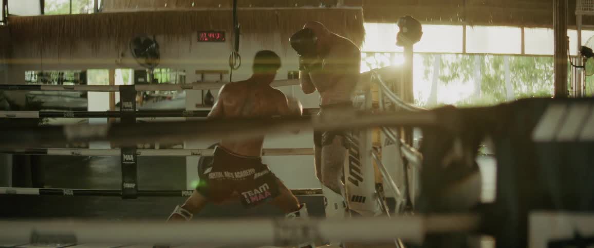 Two determined male boxers spar intensely in the ring during a slow-motion Muay Thai training session with dramatic backlighting