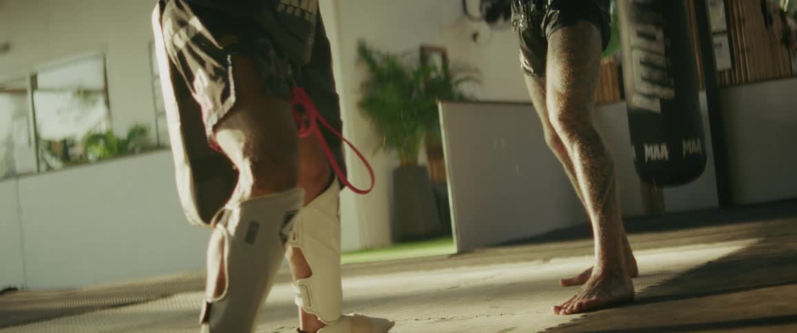 A slow-motion close-up of a tattooed martial artist's powerful kick connecting with a training pad, sending sweat flying on impact