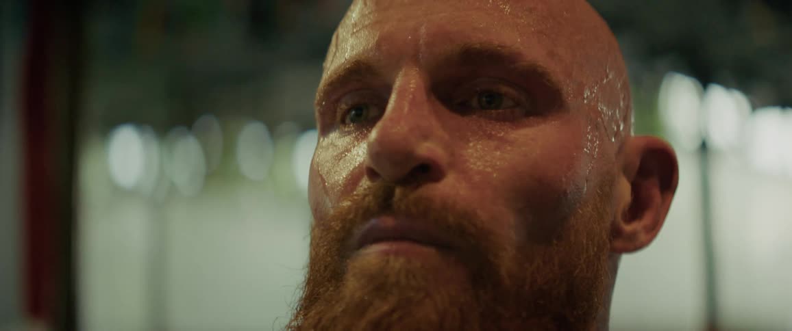 A focused, bearded fighter breathes heavily, sweat dripping from his face after an intense workout in slow motion