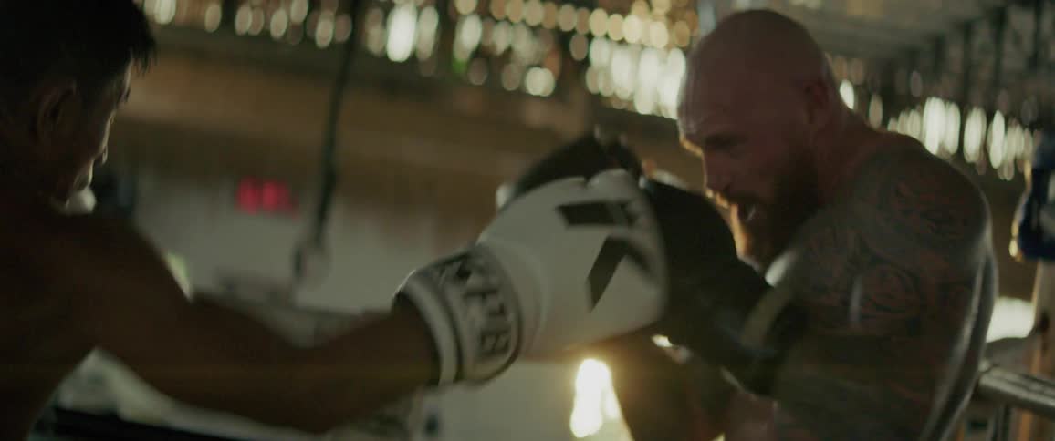 Slow-motion close-up of two tattooed boxers sparring aggressively inside a boxing ring