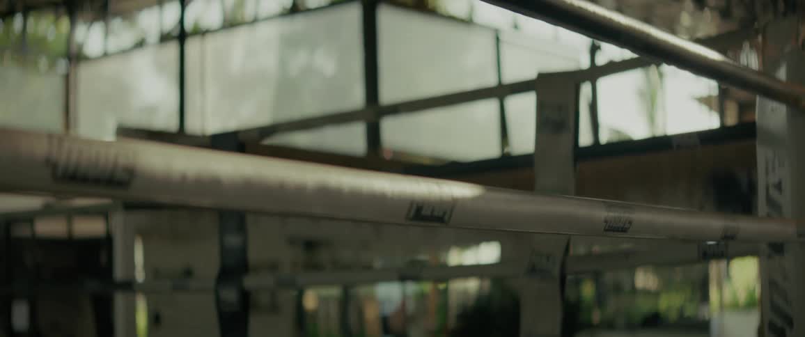 Close-up slow-motion tilt down the ropes of an empty boxing ring in a gritty gym