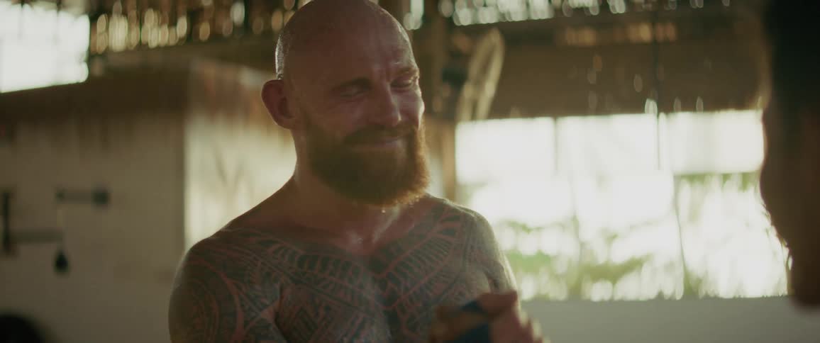 A tattooed, bearded fighter shares an emotional and joyful moment of respect and laughter with his training partner after a workout