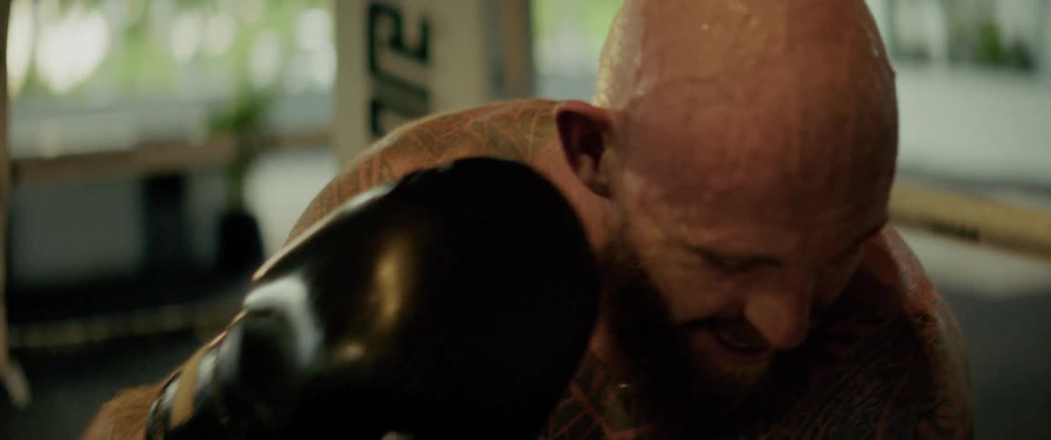 Exhausted tattooed fighter catches his breath in the boxing ring after a strenuous workout