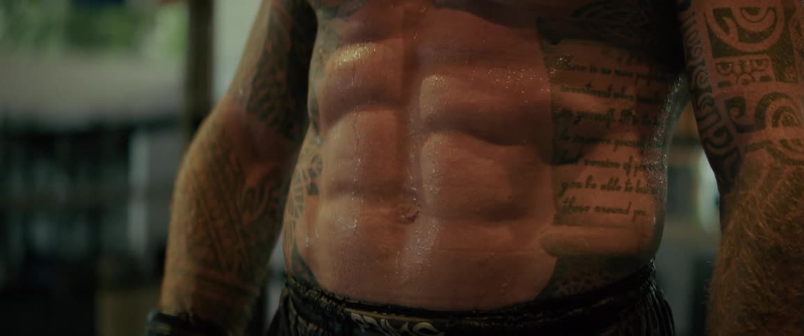 A close-up of a tattooed athlete's muscular and sweaty abs as he breathes heavily during a workout