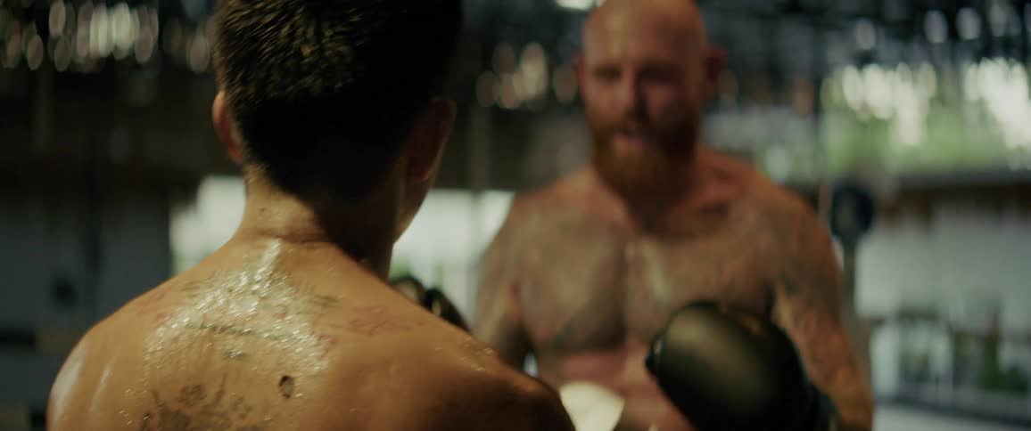 Over-the-shoulder slow motion shot of a sweaty tattooed boxer facing his muscular, bearded opponent in a boxing ring