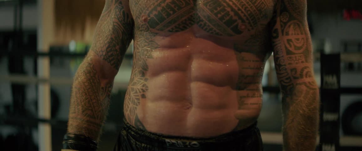 Slow-motion close-up of a muscular, heavily tattooed boxer with defined abs, breathing heavily after an intense workout