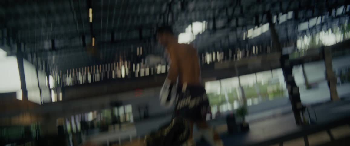 A tattooed Muay Thai fighter gets knocked down by a kick in a gritty boxing ring but slowly rises with a determined smile in slow motion