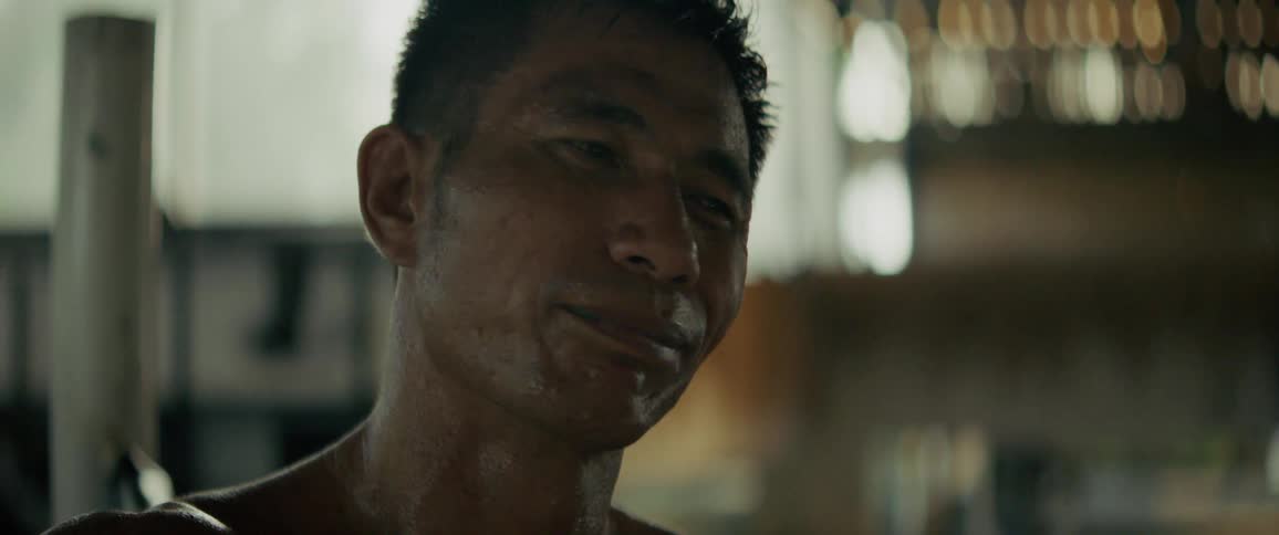 A sweaty and determined male fighter smiles with a mouthguard in, captured in a slow-motion close-up after a workout